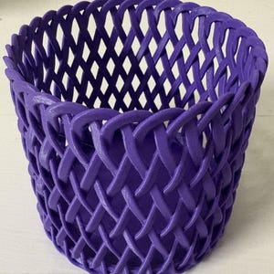 May include: A woven basket in a vibrant purple hue. The basket features a detailed, interlaced design, creating a textured surface. The open weave allows light to pass through, highlighting the intricate pattern. This decorative basket is suitable for various uses.