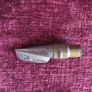 K&ouml;nnte beinhalten: Ein metallisches Werkzeug mit einer silberfarbenen Spitze und einem gerippten, messingfarbenen zylindrischen Sockel. Der silberne Teil tr&auml;gt die eingepr&auml;gte Aufschrift PAT AUG 93 und PAT GT BRITAIN. Das Objekt hat eine konische Form.