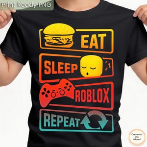 May include: Black t-shirt with a graphic design featuring a burger, a sleeping yellow cube, and a red game controller. The text reads "EAT SLEEP ROBLOX REPEAT" in a gradient of orange, red, and blue.