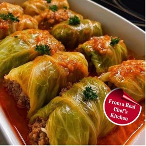 Könnte beinhalten: Nahaufnahme von gefüllten Kohlrouladen in einer weißen Auflaufform. Die grünen Kohlblätter sind mit einer herzhaften Mischung gefüllt und mit einer Tomatensauce bedeckt. Das Bild enthält den Text "From a Real Chef's Kitchen."
