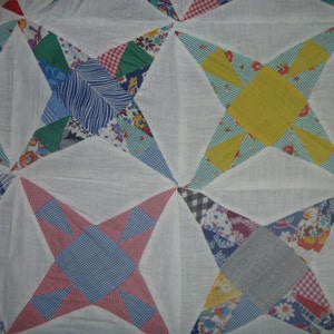 Könnte beinhalten: Eine weiße Steppdecke mit Patchwork-Muster in verschiedenen Farben und Mustern, darunter Blau, Rot, Grün, Gelb und Weiß. Die Steppdecke besteht aus Quadraten und Dreiecken, und die Muster sind in einem geometrischen Design angeordnet.