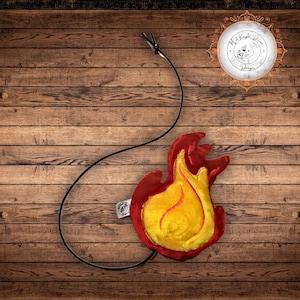 May include: A plush flame-shaped pendant featuring a bright yellow center with red stitching and a deep red outer border. The soft flame is attached to a long, thin black cord. A small white fabric tag is visible on the side of the red border.
