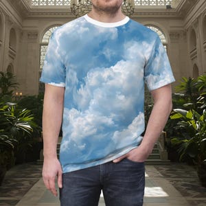 May include: A short-sleeved t-shirt featuring an all-over print of a bright blue sky filled with fluffy white clouds. The garment has a solid white crew neckline and is paired with dark blue denim jeans, creating a casual and clean appearance.