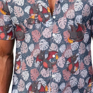 May include: A short-sleeved button-down shirt featuring a repeating pattern of small black dragon-like creatures with red wings and orange flames, interspersed with light pink and white tropical monstera leaves on a dark gray background.