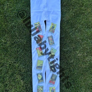 May include: White tights with colorful tarot card designs. The tights feature various tarot card illustrations in shades of red, yellow, green, and blue. The tights are displayed on a green grassy surface.