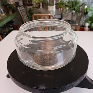 May include: A clear glass jar with a wide mouth and a rounded bottom, sitting on a black wooden pedestal.