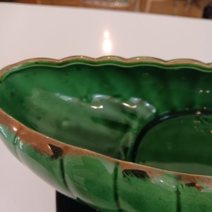 May include: A large, green ceramic bowl with a gold rim. The bowl has a wavy edge and a slightly textured surface.
