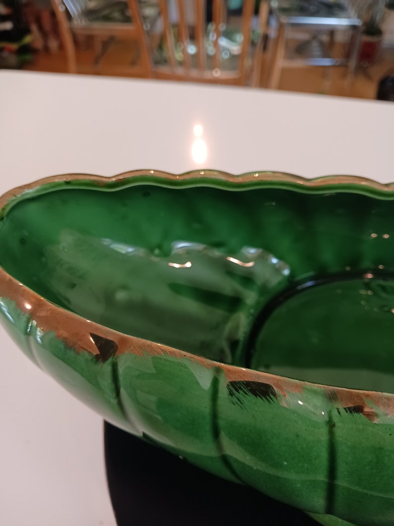 May include: A large, green ceramic bowl with a gold rim. The bowl has a wavy edge and a slightly textured surface.