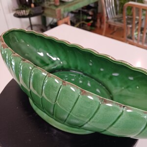 May include: A large, green ceramic planter with a wavy rim and a ribbed design. The planter is empty and sitting on a black surface.