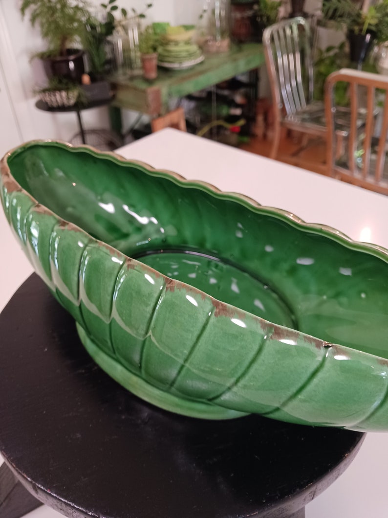 May include: A large, green ceramic planter with a wavy rim and a ribbed design. The planter is empty and sitting on a black surface.