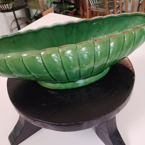 May include: A green ceramic planter with a ribbed design sits on a black wooden stool with three legs.