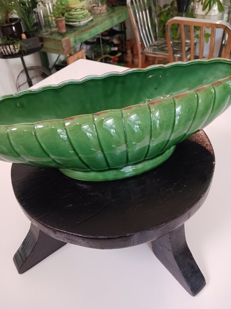 May include: A green ceramic planter with a ribbed design sits on a black wooden stool with three legs.