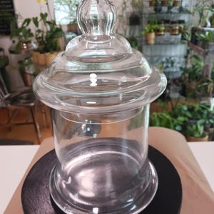 May include: A clear glass jar with a lid. The jar has a wide mouth and a round base. The lid has a knob on top.