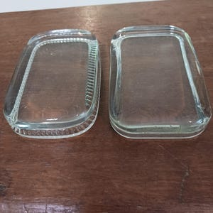 May include: Two clear glass rectangular dishes with slightly rounded edges. The dishes are on a wooden surface.