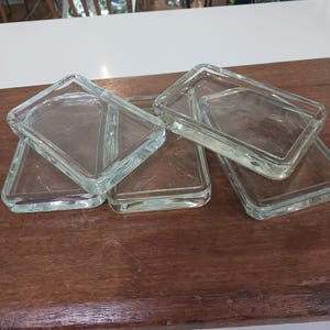 Può includere: Quattro vassoi rettangolari in vetro trasparente impilati uno sopra l'altro su una superficie in legno.
