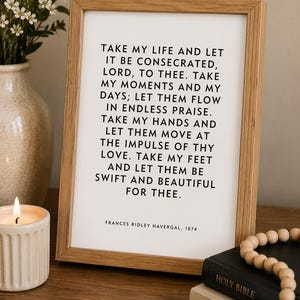 May include: A rectangular light wood frame containing a white print with black text that reads: TAKE MY LIFE AND LET IT BE CONSECRATED, LORD, TO THEE. TAKE MY MOMENTS AND MY DAYS; LET THEM FLOW IN ENDLESS PRAISE. FRANCES RIDLEY HAVERGAL, 1874.