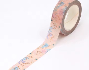 May include: A roll of decorative washi tape featuring a celestial design. The tape has a light pink background with gold, blue, and purple accents. The design includes constellations, flowers, and other celestial elements. Perfect for scrapbooking and crafts.