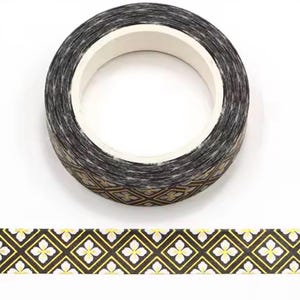 May include: A roll of decorative washi tape with a black and gold geometric pattern. The tape features a repeating design of gold diamonds with white floral accents. The tape is on a white background.