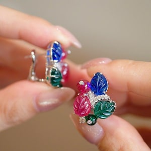May include: A pair of earrings featuring carved leaf-shaped gemstones in vibrant blue, green, and red hues. Each earring is accented with small, clear, round-cut stones set in a silver-toned metal frame, creating a cluster of colorful botanical shapes.