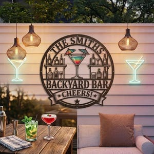 以下が含まれることがあります： 「THE SMITHS BACKYARD BAR CHEERS！」の文字が入った金属製の看板には、カクテルグラスのデザインが施されています。 ネオンのマティーニグラスライトやペンダントライトなど、バーをテーマにした装飾が施されています。 カクテルは木製のテーブルに置かれています。