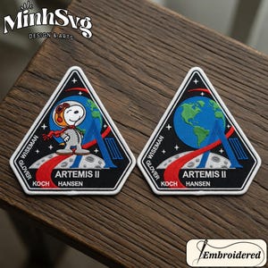 May include: Two embroidered patches with a triangular design. One features Snoopy in an astronaut suit on the moon, the other shows Earth and the Artemis II mission logo. The patches have the names of the astronauts and the text "ARTEMIS II".