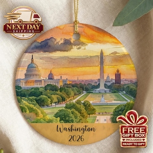 May include: A round ceramic ornament featuring a watercolor illustration of the Washington D.C. skyline at sunset, including the Capitol building and Washington Monument. The text Washington 2026 is printed in black at the bottom of the ornament.