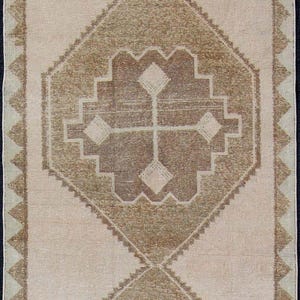 Könnte beinhalten: Ein rechteckiger Läufer mit hellbeigem Hintergrund und zwei großen, mittig platzierten braunen Rautenmotiven. Jede Raute enthält ein kleineres geometrisches Kreuzmuster. Der Rand besteht aus einem wiederkehrenden braunen Sägezahnmuster.
