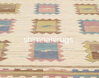 Könnte beinhalten: Cremefarbener Teppich mit einem sich wiederholenden Muster aus quadratischen Formen in Blau-, Rosa- und Brauntönen. Der Teppich hat einen Rand mit geometrischen Designs und Fransen. Der Text "shimnanirugs" ist sichtbar.