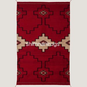 Pode incluir: Um tapete retangular vermelho com um padrão geométrico. O tapete apresenta um design central em bege e preto, com padrões escalonados repetidos e motivos em forma de diamante. O texto "shimnanirugs" é visível.