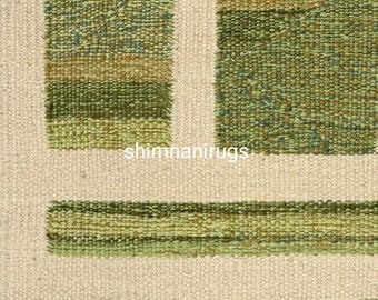 May include: Close-up of a woven rug with a textured design. The rug features alternating stripes of green and beige, with the text "shimnanirugs" visible. The rug's pattern includes horizontal and vertical lines, creating a geometric effect.