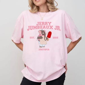 Puede incluir: Camiseta rosa claro con el texto "JERRY JUMBEAUX JR." en rosa, y una ilustraci&oacute;n de un elefante sosteniendo un helado rojo. El texto "EST. 2016 ZOOTOPIA" tambi&eacute;n est&aacute; impreso en la camiseta.