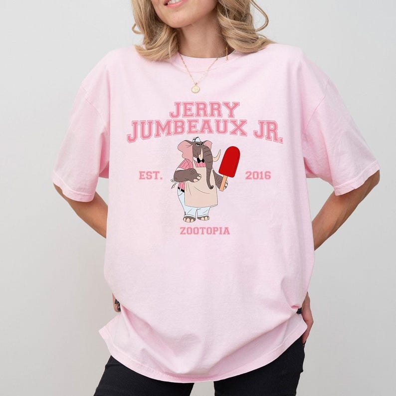 Puede incluir: Camiseta rosa claro con el texto "JERRY JUMBEAUX JR." en rosa, y una ilustraci&oacute;n de un elefante sosteniendo un helado rojo. El texto "EST. 2016 ZOOTOPIA" tambi&eacute;n est&aacute; impreso en la camiseta.