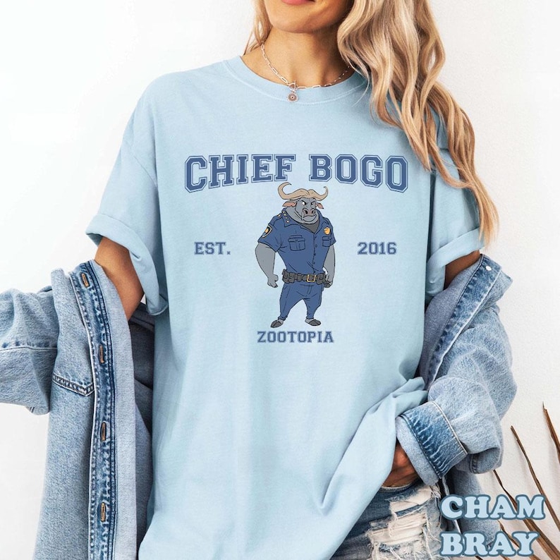 Puede incluir: Camiseta azul claro con el personaje de Chief Bogo de Zootopia. El dise&ntilde;o incluye el texto "CHIEF BOGO" sobre una ilustraci&oacute;n del personaje con uniforme de polic&iacute;a, con "EST. 2016" y "ZOOTOPIA" debajo.