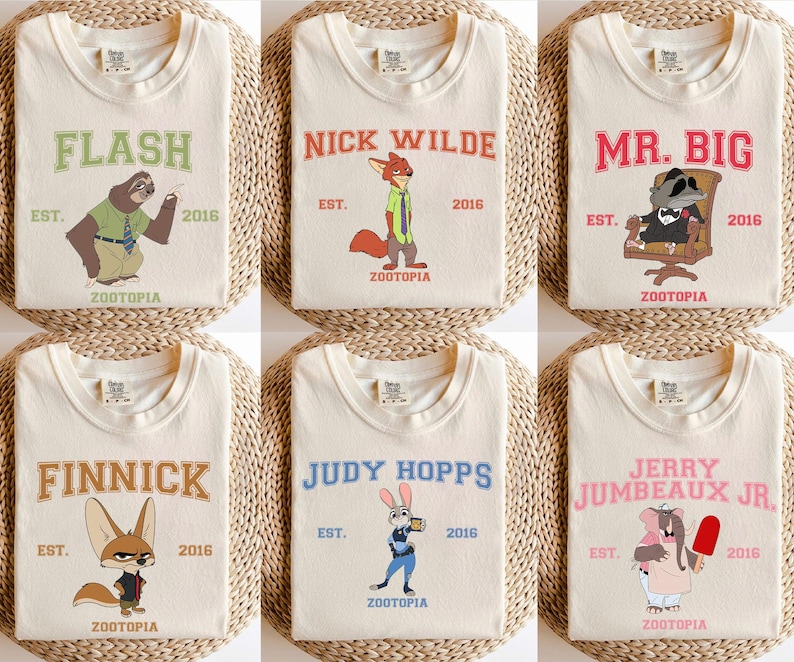 Puede incluir: Camisetas color crema con personajes de Zootopia. Cada camiseta muestra el nombre de un personaje en un color diferente, junto con el texto "EST. 2016" y la palabra "ZOOTOPIA". Los personajes incluyen a Flash, Nick Wilde, Mr. Big, Finnick, Judy Hopps y Jerry Jumbeaux Jr.