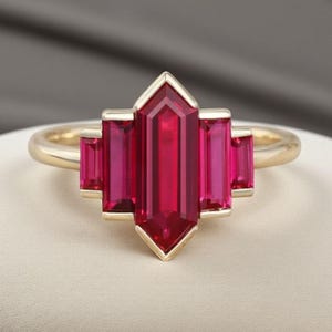 Peut inclure: Une bague en or ornée d'une pierre rouge centrale allongée, flanquée de quatre pierres rouges rectangulaires plus petites. La bague a un design géométrique.