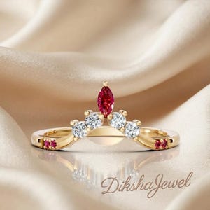May include: A gold V-shaped ring featuring a central marquise-cut red gemstone, flanked by four round white stones and two smaller red stones on each side of the band. The text DikshaJewel is visible in the lower right corner of the image.