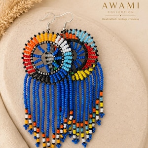 May include: A pair of circular drop earrings featuring intricate beadwork in vibrant shades of blue, yellow, orange, red, white, and black. The design includes a central wheel pattern with long, dangling beaded fringe strands and silver-tone hooks.