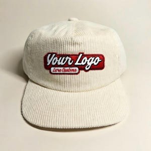 May include: An off-white corduroy baseball cap featuring an embroidered patch on the front. The patch has a red background with white text that reads Your Logo and smaller text below that reads Lara Customs in a script font style.
