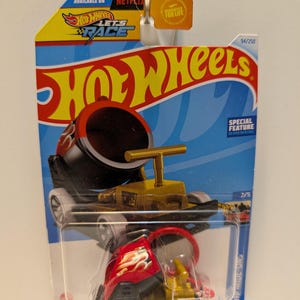 Könnte beinhalten: Ein Hot Wheels Spielzeugauto in einer transparenten Kunststoffverpackung. Das Auto ist rot und schwarz mit Flammengrafiken und einem goldfarbenen Oberteil. Die Verpackung zeigt das Hot Wheels-Logo, den Text "LET'S RACE" und "AVAILABLE ON NETFLIX".
