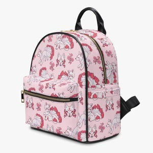 May include: A pink backpack featuring a repeating pattern of white foxes with red tails and pink flowers. It has black zippers, a black handle, and a black adjustable strap. The bag includes a front pocket with a zip.