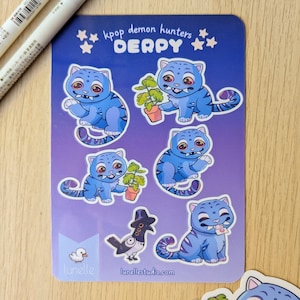 May include: A sheet of stickers featuring blue cartoon cat-like creatures with red eyes and striped tails. Some cats hold plants, a letter, or are near a crow wearing a hat. The text "kpop demon hunters DERPY" is at the top.
