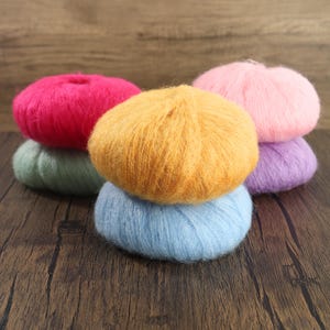 May include: A collection of colorful yarn balls in shades of pink, yellow, blue, green, and purple. The yarn balls are arranged on a dark wooden surface, creating a visually appealing display for crafting projects.