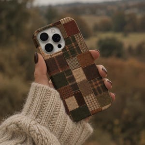 May include: A smartphone case featuring a patchwork design of various fabric textures in shades of brown, tan, olive green, and cream. The case has a rectangular shape with rounded corners and a cutout for a triple-lens camera system on the back.