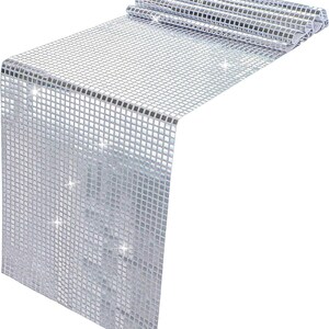 May include: A silver table runner with a square, mosaic-like pattern. The runner is partially rolled up at the top, revealing the underside. The surface reflects light, creating a sparkling effect. This decorative piece is suitable for special events and home decor.
