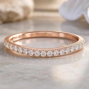 Op de afbeelding: Roségouden bandring met een doorlopende rij kleine, ronde, heldere edelstenen. De ring ligt op een reflecterend oppervlak. De tekst "VowandCarat" is zichtbaar op de ring.