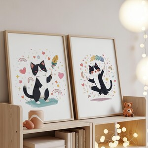 Puede incluir: Dos impresiones artísticas enmarcadas con ilustraciones de gatos en blanco y negro. Un gato sostiene una pluma, el otro baila con una pluma arcoíris. Las impresiones incluyen corazones, arcoíris y estrellas, en marcos de madera clara.