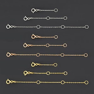 May include: A collection of necklace chain extenders in silver, rose gold, and gold tones. Each extender features a lobster clasp on one end, a small circular ring in the middle, and a jump ring on the other end. The extenders vary in length.