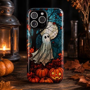 May include: A smartphone case featuring a stained-glass style illustration of a white ghost floating in front of a large full moon, surrounded by dark blue tree branches, red autumn leaves, and several orange jack-o'-lanterns on the ground.