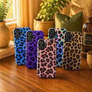 May include: A collection of phone cases with leopard print designs in various colors, including blue, purple, pink, and brown. The cases are arranged on a wooden surface, showcasing their unique patterns and textures.