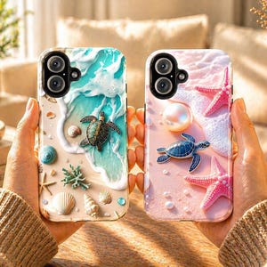 May include: Two phone cases with ocean-themed designs. One case features a sea turtle on a beach with waves, shells, and coral. The other case has a sea turtle, starfish, and pearl on a pink beach background. Both cases have a camera lens cutout.